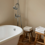Pommeau de douche chromé au-dessus d'une baignoire, serviettes pliées sur un tabouret en bois
