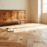 Parquet ancien en chêne couleur miel dans un salon rustique, avec pot de cire d'abeille et chiffons posés au sol