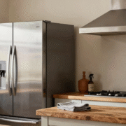 Frigo et hotte en inox brossé impeccables dans une cuisine rustique, avec microfibre et vaporisateur posés sur le plan de travail