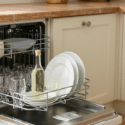 Lave-vaisselle ouvert sur des verres étincelants, vinaigre blanc et brosse posés à côté