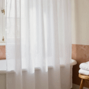 Salle de bains claire avec un rideau de douche blanc propre, tiré et déployé au-dessus de la baignoire