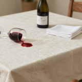 Verre de vin rouge renversé sur une nappe blanche, avec une bouteille d'eau gazeuse prête pour le détachage
