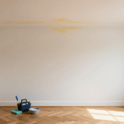 Angle de mur et plafond blanc marqué d'une auréole jaunâtre, avec un petit matériel de nettoyage posé au sol