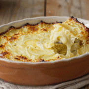 Gratin de pommes de terre bien doré dans un plat en terre cuite, une part soulevée montrant les couches fondantes