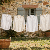 Chemises sur cintres en bois et linge blanc séchant sur un fil dans un jardin ensoleillé, panier en osier posé dans l'herbe