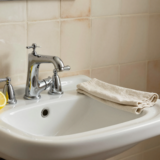 Robinet chromé brillant sur un lavabo en céramique, avec vinaigre blanc et demi-citron posés à côté