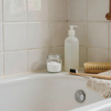 Bicarbonate, vinaigre blanc et brosses posés au bord d'une baignoire pour nettoyer les joints de carrelage