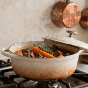 Cocotte en fonte émaillée mijotant à couvercle entrouvert sur une cuisinière, bœuf aux carottes et thym à l'intérieur