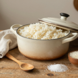 Casserole de riz basmati aux grains détachés sur une table en bois, avec torchon en lin et bols de riz cru