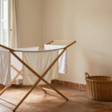 Étendoir en bois avec linge blanc bien espacé près d'une fenêtre ouverte dans une buanderie lumineuse